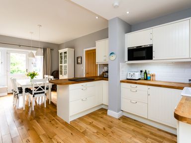 A kitchen with white cabinets wooden countertops and a dining table with chairs at The Beach House Alnmouth
