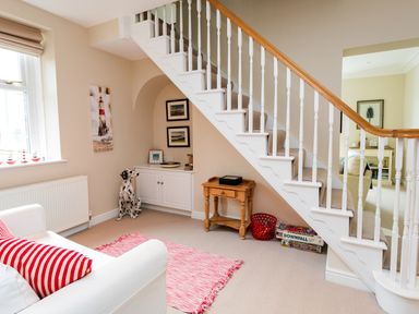 A sitting area with a white sofa and red striped cushions under a staircase with board games and a wooden side table at The Beach House Alnmouth