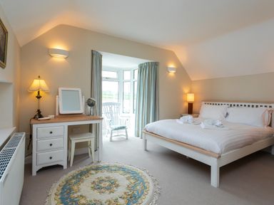 A bedroom with a white bed and pillows a dressing table with a stool and lamps a chair in front of a window at The Beach House Alnmouth