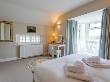 A bedroom with a bed, a dressing table with a lamp, a round rug, and a white rocking chair by a window at The Beach House Alnmouth