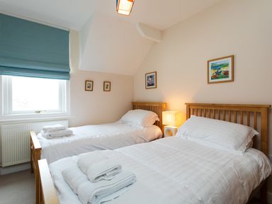 A bedroom with two single beds with white bedding and folded towels by a window with a blue blind at The Beach House Alnmouth