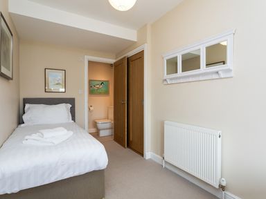 A bedroom with a single bed and folded towels on the bed a door leading to an en suite bathroom with a toilet and bird painting on the wall at The Beach House Alnmouth