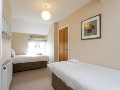 A bedroom with two single beds a wooden door a window and wall decorations at The Beach House Alnmouth