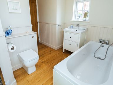 A bathroom with a toilet, sink, bathtub, wooden floor and a small window at The Beach House, Alnmouth