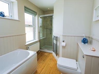 A bathroom with a bathtub, shower, toilet, radiator, and window at The Beach House Alnmouth