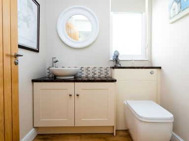 A bathroom with a sink, vanity cabinet, toilet, mirror, and window at The Beach House, Alnmouth