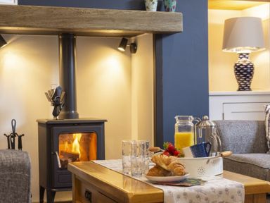 A living room with a wood stove fireplace and a coffee table with croissants orange juice and a coffee pot Wisteria Cottage in Warkworth