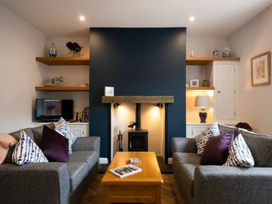 A living room with two gray sofas and a wooden coffee table facing a fireplace with shelves on either side at Wisteria Cottage in Warkworth