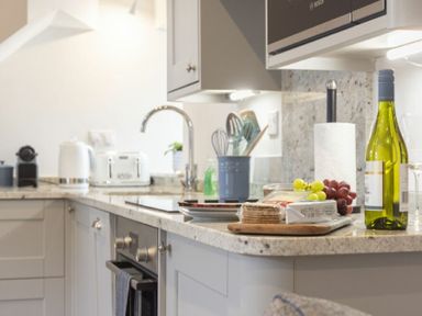 A kitchen counter with a wine bottle grapes a roll of paper towels kitchen utensils and a sink at Wisteria Cottage in Warkworth