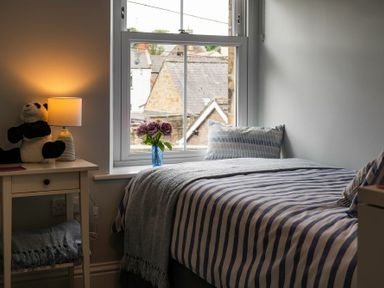 A bedroom with a bed striped bedding a bedside table with a lamp and a stuffed panda at Wisteria Cottage in Warkworth