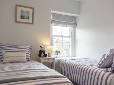 A bedroom with two single beds striped bedding a nightstand with a lamp and a panda toy at Wisteria Cottage in Warkworth