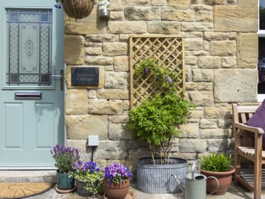 A stone wall with a green door and potted plants outside Wisteria Cottage in Warkworth