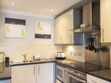 A kitchen with cream cabinets black countertops stainless steel appliances and two paintings of pears on the wall at Puffin View in Seahouses