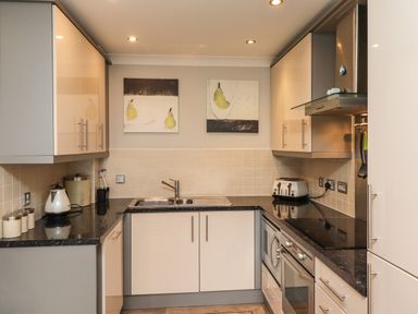 A kitchen with cream cabinets black countertops a toaster kettle and oven at Puffin View in Seahouses