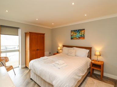 A bedroom with a large bed, bedside tables with lamps, a wooden wardrobe, a chair, and a painting on the wall at Puffin View in Seahouses