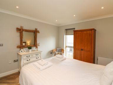 A bedroom with a bed with folded towels a wooden wardrobe a white dresser with a mirror and a chair at Puffin View in Seahouses