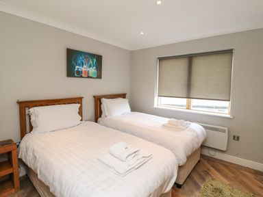 A bedroom with two single beds wooden headboards a window with gray blinds and a painting above the beds at Puffin View in Seahouses