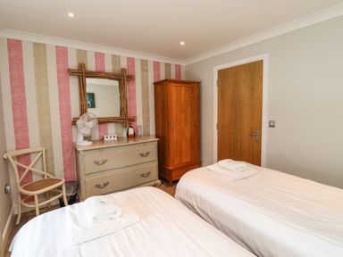 A bedroom with two single beds a wooden wardrobe a dresser with a fan and a chair at Puffin View in Seahouses