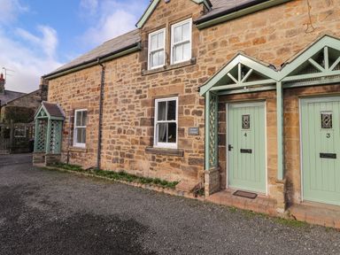A stone cottage exterior with two green doors numbered 3 and 4 and windows at Willow Cottage in Lesbury