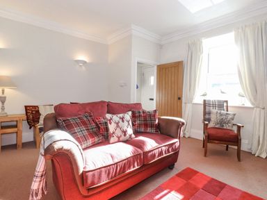 A living room with a red sofa and matching armchair near a window with curtains at Willow Cottage in Lesbury