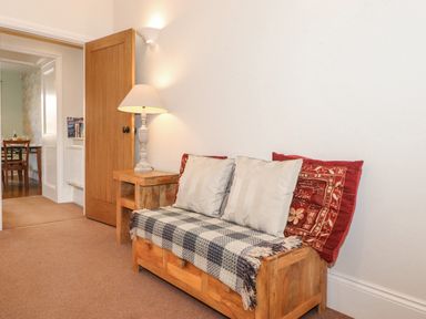 A hallway with a wooden bench with cushions and a side table with a lamp at Willow Cottage in Lesbury