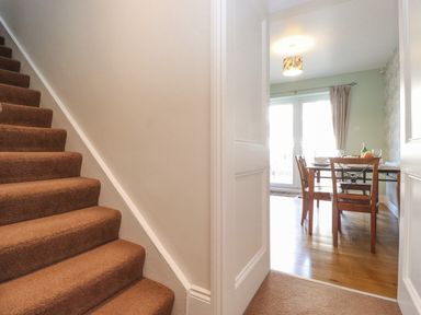 A staircase with brown carpet next to a dining room with wooden chairs and table at Willow Cottage in Lesbury