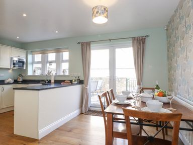 A kitchen and dining area with a wooden table set for a meal next to glass doors and a white kitchen counter at Willow Cottage in Lesbury
