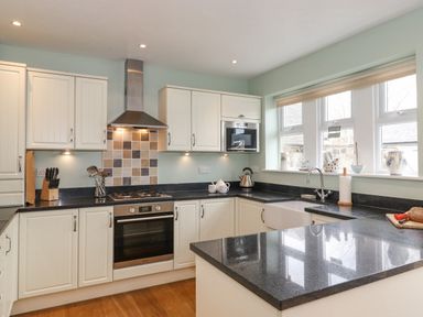A kitchen with white cabinets black countertops a stove oven sink and windows at Willow Cottage in Lesbury