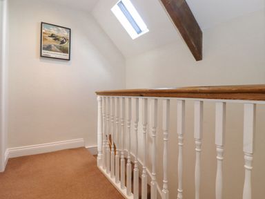 A staircase landing with a wooden handrail white balusters skylight window and a framed Northumberland print on the wall at Willow Cottage in Lesbury