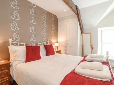A bedroom with a white metal bed frame red pillows bedside tables with lamps a standing mirror and folded towels at Willow Cottage in Lesbury