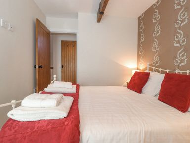 A bedroom with a bed with red pillows and folded towels at Willow Cottage in Lesbury
