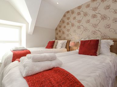 A bedroom with two single beds with red throws and cushions and floral wallpaper at Willow Cottage in Lesbury