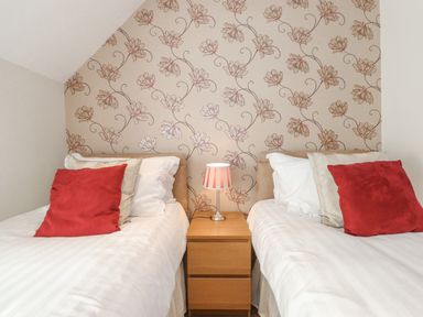 A bedroom with two single beds with red cushions and a wooden nightstand with a lamp at Willow Cottage in Lesbury