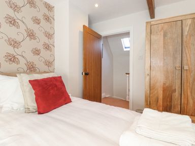 A bedroom with a bed with pillows and folded towels and a wooden wardrobe at Willow Cottage in Lesbury