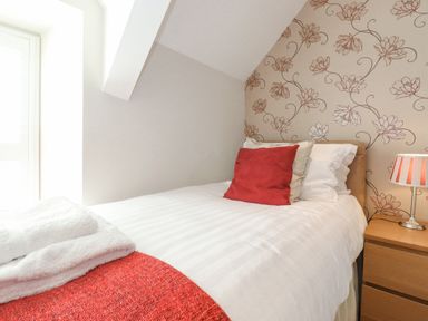 A bedroom with a single bed red and white pillows a bedside table with a lamp and towels on the bed at Willow Cottage in Lesbury