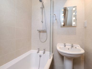 A bathroom with a bathtub shower combination a pedestal sink and a mirror at Willow Cottage in Lesbury