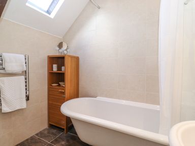 A bathroom with a bathtub wooden cabinet towels on a rack and a skylight at Willow Cottage in Lesbury