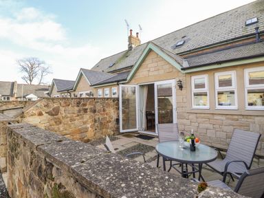 An outdoor patio area with glass table and chairs next to a stone house at Willow Cottage in Lesbury