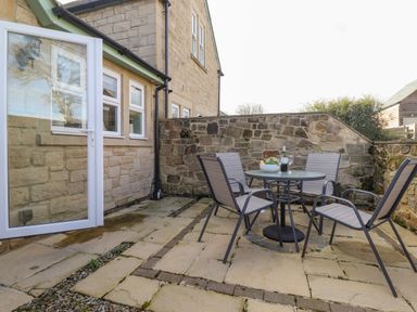 An outdoor patio area with a round glass table and four chairs next to a stone wall at Willow Cottage in Lesbury
