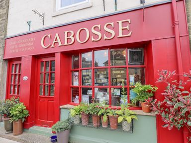 A red storefront with plants outside and signs for cakes chocolates gifts and souvenirs at Cabosse