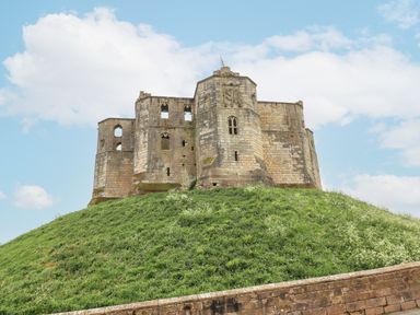 An old stone castle on a grassy hill under a blue sky at Westhill House in Warkworth