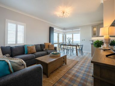 A living room with a gray sofa an armchair a wooden coffee table and a dining table with chairs at Keildon in Seahouses