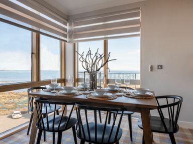 A dining area with a wooden table set for six with black chairs and a view of the sea at Keildon in Seahouses