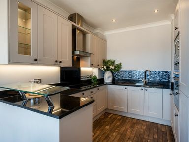 A kitchen with black countertops gray cabinets glass shelf and wooden floor at Keildon in Seahouses