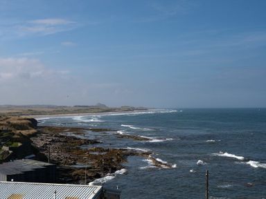 A coastal view showing the ocean with waves hitting a rocky shoreline and a distant landmass at Keildon in Seahouses