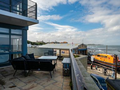 A balcony with outdoor furniture overlooking a coastal area and a bright orange boat at Keildon in Seahouses