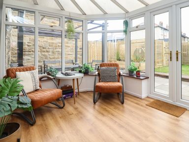A conservatory with two brown chairs small white table and plants at Muscle Shoals in Seahouses