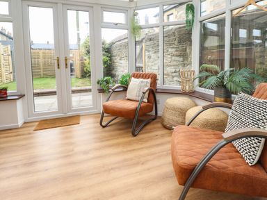 A conservatory with two orange chairs and plants by windows at Muscle Shoals in Seahouses