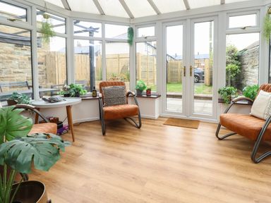 A conservatory with three armchairs a white round table hardwood flooring and plants at Muscle Shoals in Seahouses