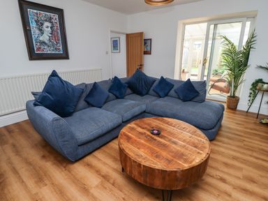 A living room with a blue sectional sofa and a round wooden coffee table at Muscle Shoals in Seahouses